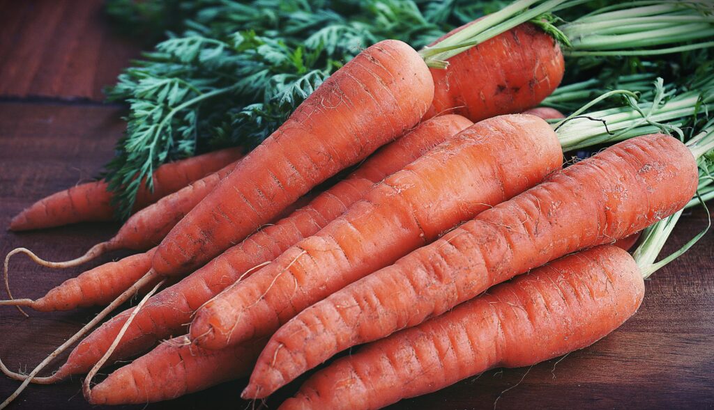 Close-up of fresh organic carrots with greens on a wooden surface, showcasing vibrant orange color.